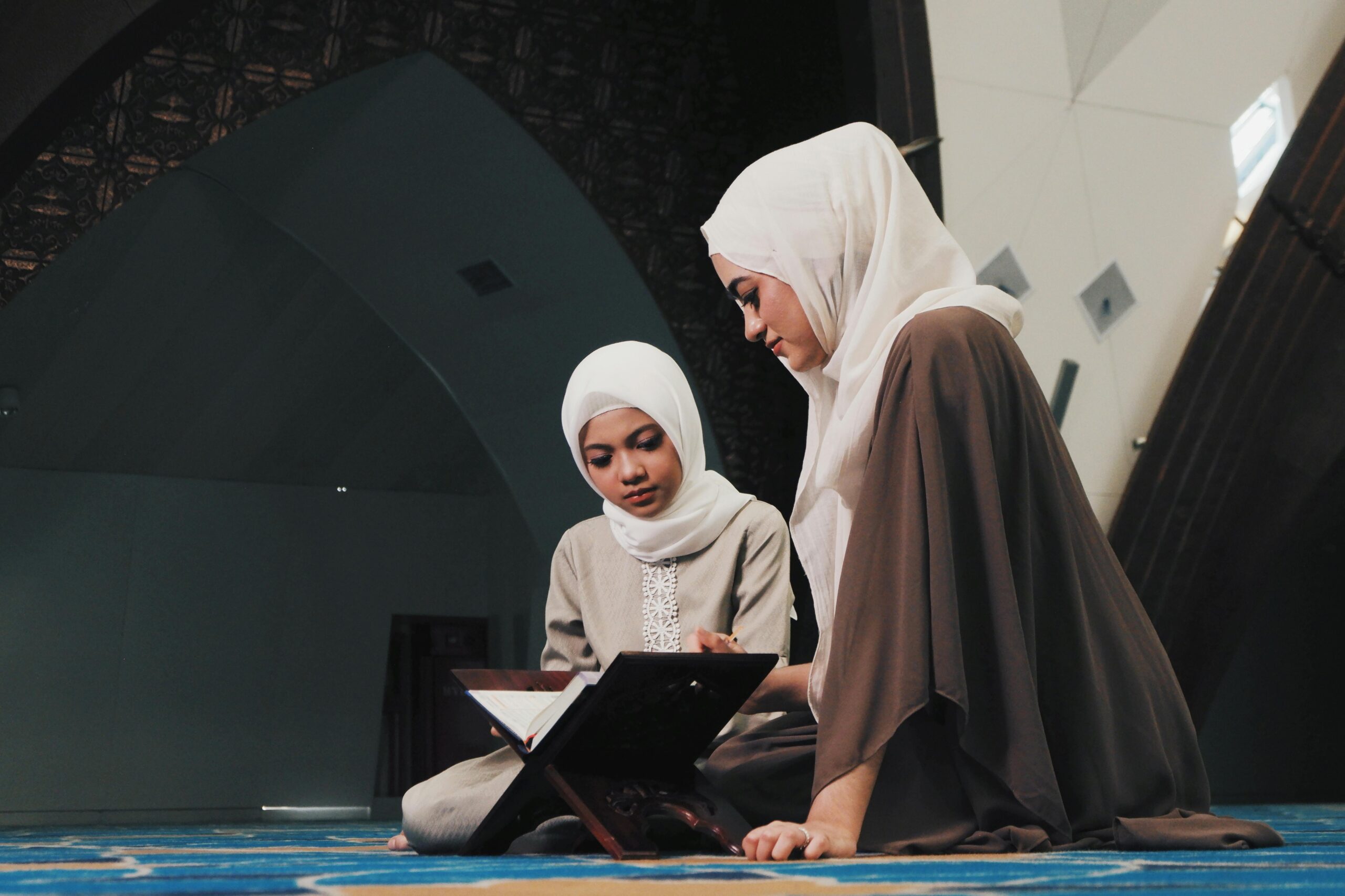 Two Muslim women reading the Quran in a serene mosque environment in Bandung, Indonesia.