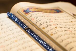 Detailed image of an open Quran with an ornate blue beaded bookmark, showcasing sacred script.