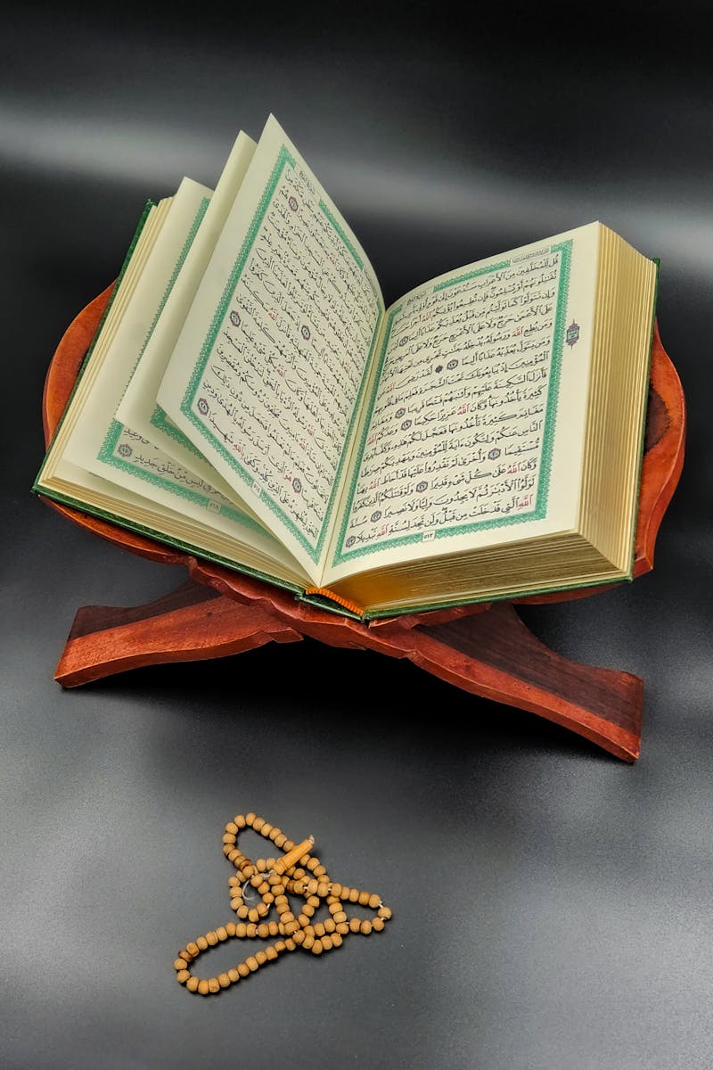 An open Quran displayed on a wooden stand with prayer beads, symbolizing spirituality.