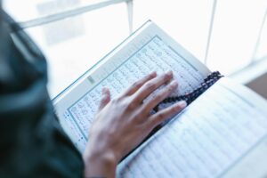 A person reading the Quran, highlighting spirituality and worship with prayer beads.