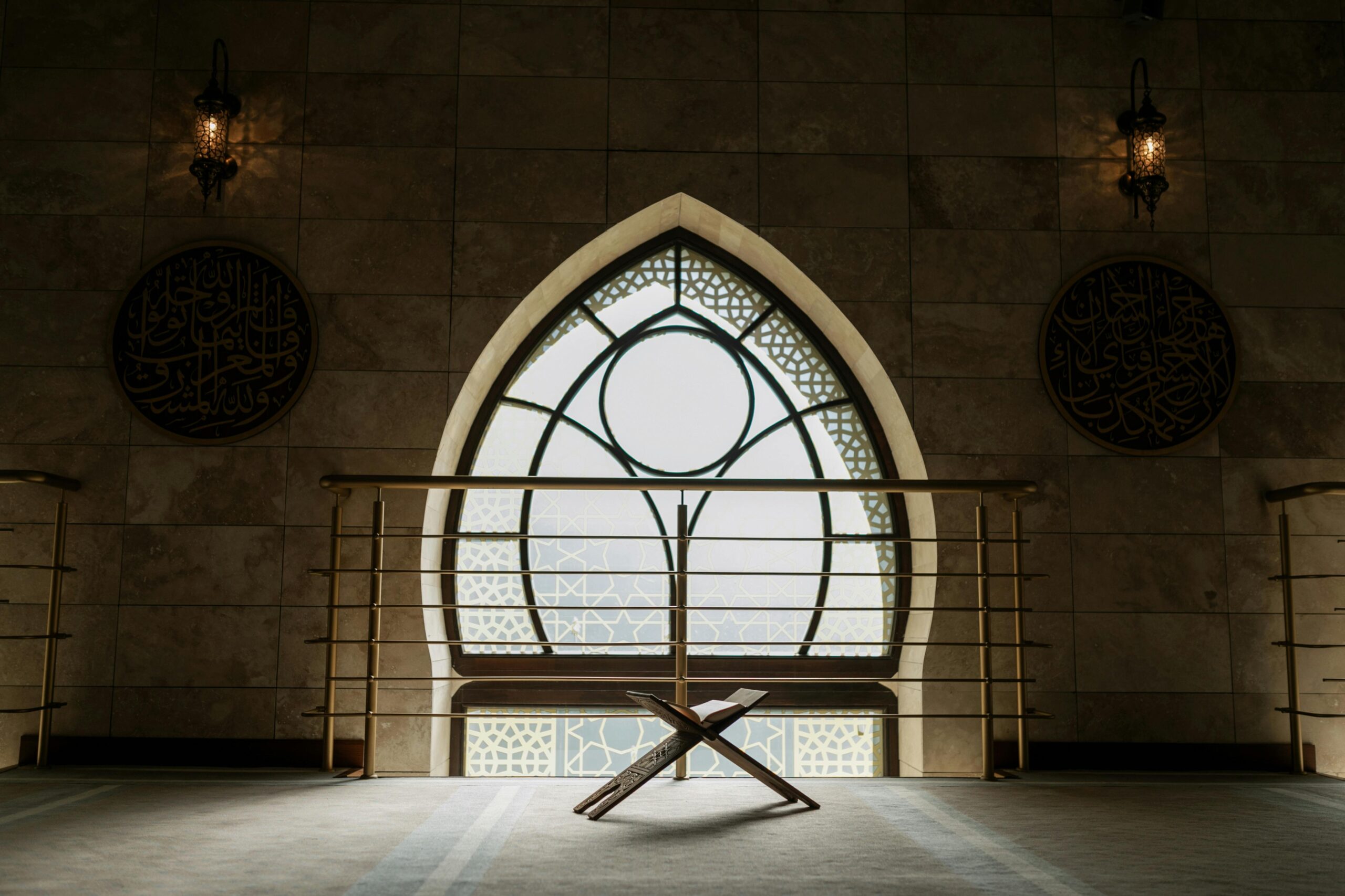A peaceful mosque interior featuring a backlit window, rehal stand, and intricate architecture.