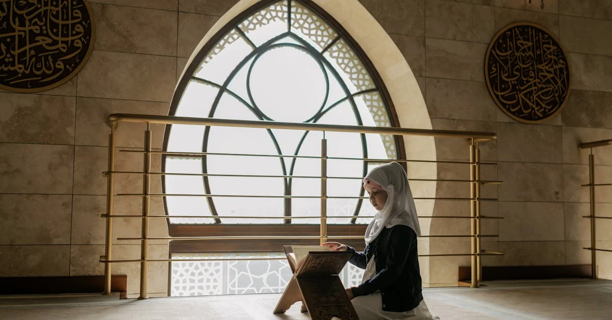 A woman in hijab prays and reads the Quran in a beautifully lit mosque interior.