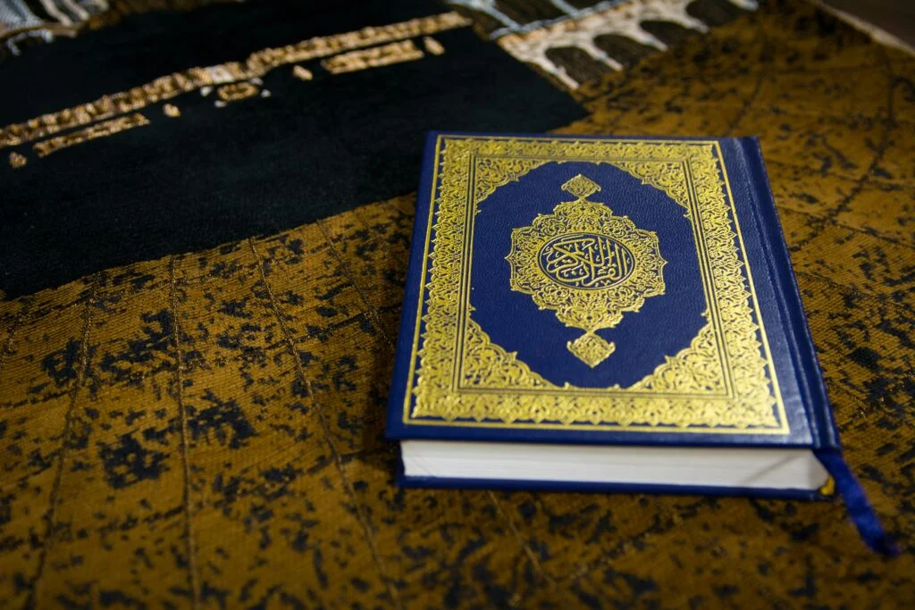 Beautiful Quran with intricate Arabic calligraphy on a textured prayer rug.